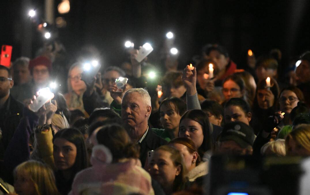 Mourners use phone lights and candles. Picture by Lachlan Bence
