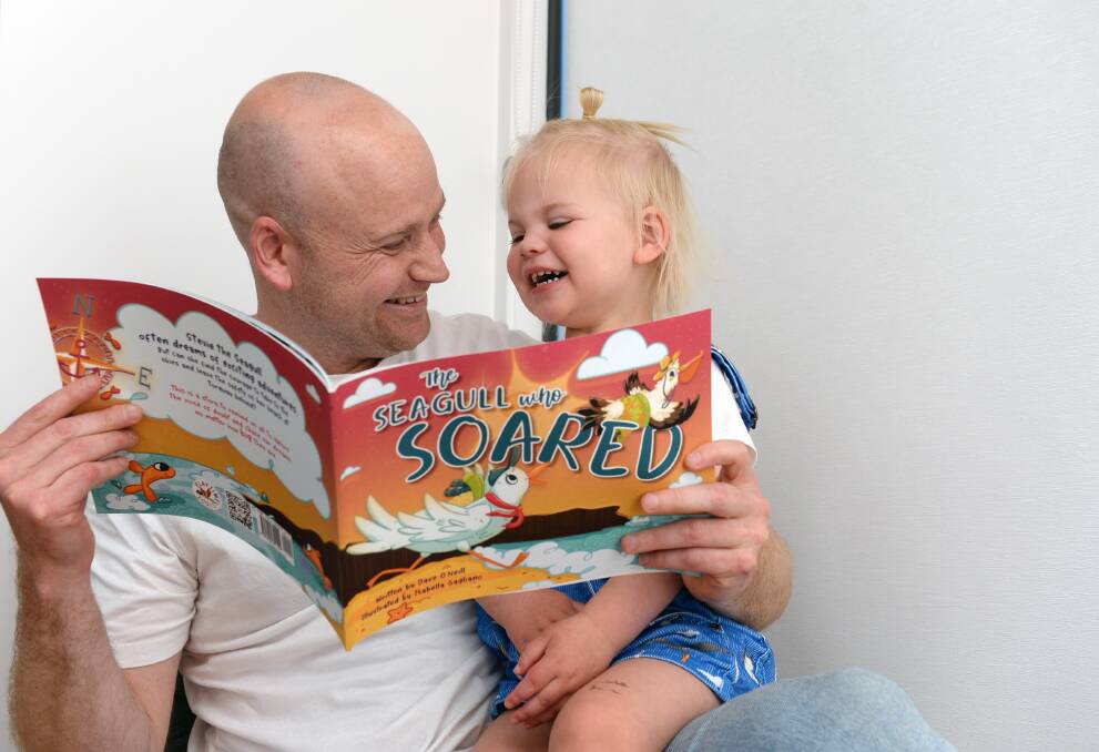 Ballarat writer Dave O'Neill shares his newly published first book The Seagull who Soared with two-year-old daughter Stevie, in seagull overalls, ahead of Clunes Booktown Festival. Picture by Kate Healy