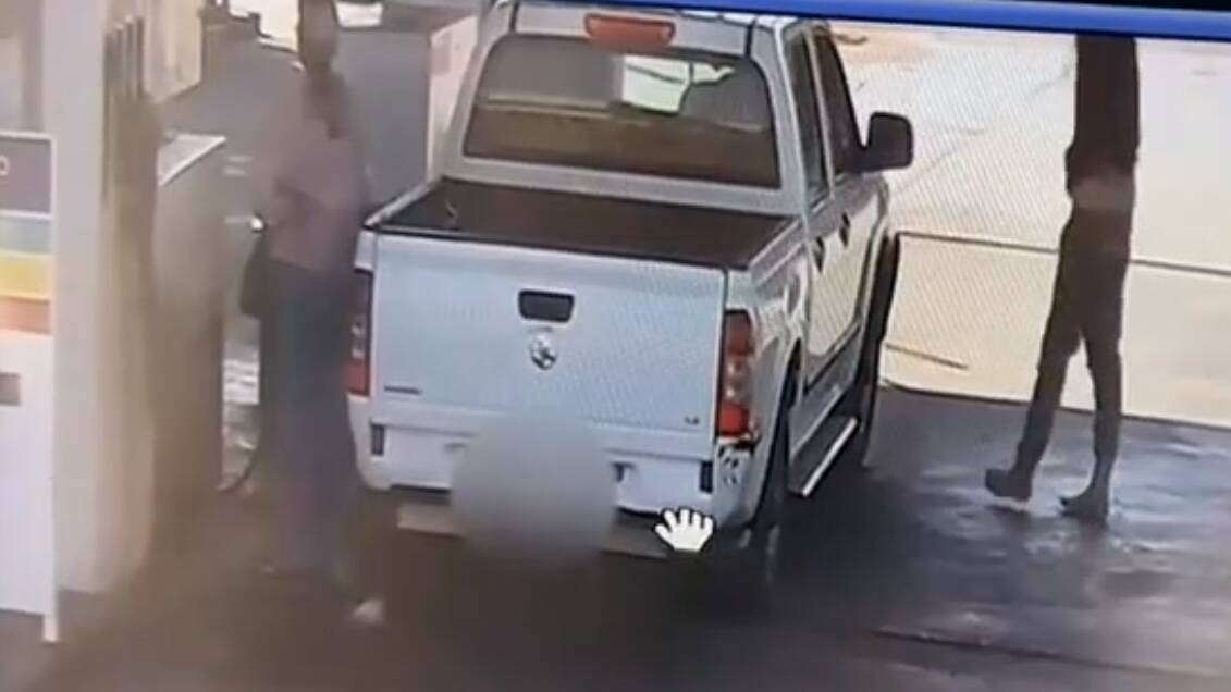 The man approaches the car while it's being filled up.